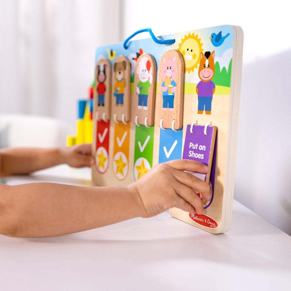 Preschool child hand flipping a bungee hinged wooden block to reveal a gold star icon on the chart